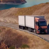 A Renault Trucks T tractor-trailer is traveling along a winding road overlooking a mountain lake.
